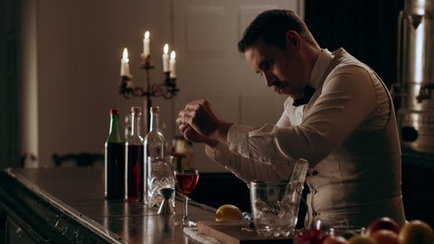 Vintage style bartender garnishing a negroni cocktail with a lemon peel for serving in interior classy bar with soft interior lighting. Medium shot on 4k RED camera on a gimbal.