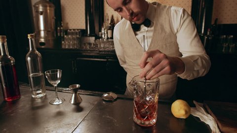 Classic bartender stirring liquor in a tall glass with a long spoon in interior classy bar with soft interior lighting. Medium shot on 4k RED camera on a gimbal.