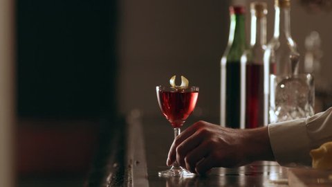 Old school bartender garnishing a negroni cocktail with a lemon peel for serving in interior classy bar with soft interior lighting. Close up shot on 4k RED camera on a gimbal.