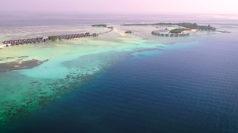 4K Aerial Video of a Small Tropical Island in Maldives Island. Palm Tree on the Sandbank. Top View of the Tropical Lagoon Sea Surface. Luxury 5 Star Resort Hotel. Water Bungalow hut Relaxing Holiday
