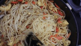 Stir frying noodles with vegetables and chicken slices in wok. Overhead shot