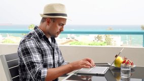 Businessman on balcony at tropical resort work on laptop. Young professional male freelancer have video chat via messenger app on computer from remote home office. Smile wave hand in greeting