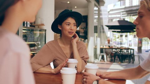 Three millennial friends chat seriously about life events while sipping coffee outside a coffee shop in Australia during the day. Medium to closeup shot with 4K RED camera.