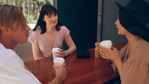 Millennial man picks up to-go coffee cups and joins two friends outside a cafe in Australia during the day. Medium to closeup shot with 4K RED camera.
