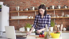 Woman watching a video tutorial on a laptop in the kitchen how to cook a dish
