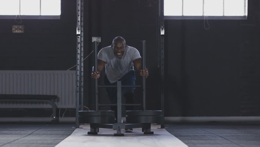 African American male pushing weight sled in gym to build leg muscles