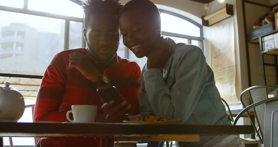 Happy african-american couple using mobile phone in cafe 4k