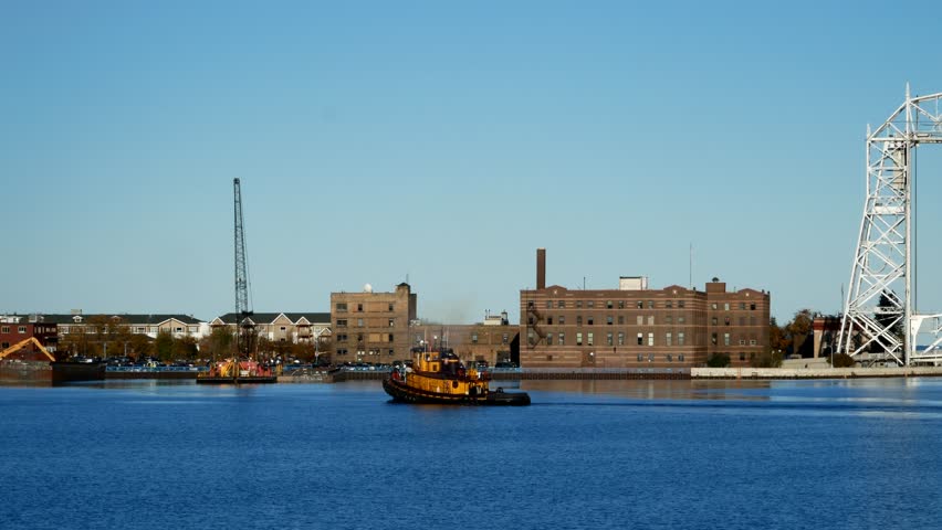 Yellow tug boat sails in Duluth Minnesota Harbor near the iconic aerial lift bridge on a sunny afternoon