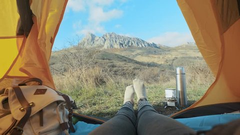 Camping woman lying in tent Close up of Girl feet wearing hiking boots relaxing on vacation. From the tent view of the big mountains. Hiking lifestyle during summer. Traveling alone in the mountains