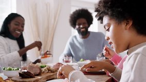 Tween black boy sitting at the dinner table eating Sunday lunch with his family, side view, selective focus - Powered by Shutterstock - Get 15% off with code: PIKWIZARD15