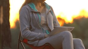 Young female in sportswear working on tablet pc in park, sitting near tree, app