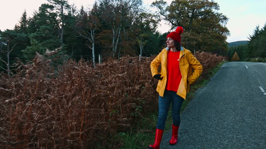 Woman walks and enjoy beautiful view of autumn in Wicklow mountains.She wear yellow raincoat and red woolen hat. Camera follows her. 4K