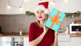 beautiful white girl in hat and red dress with a Christmas gift box in kitchen at home