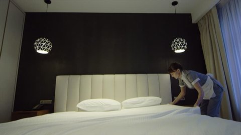 Chambermaid Makes Bed In Hotel Bedroom