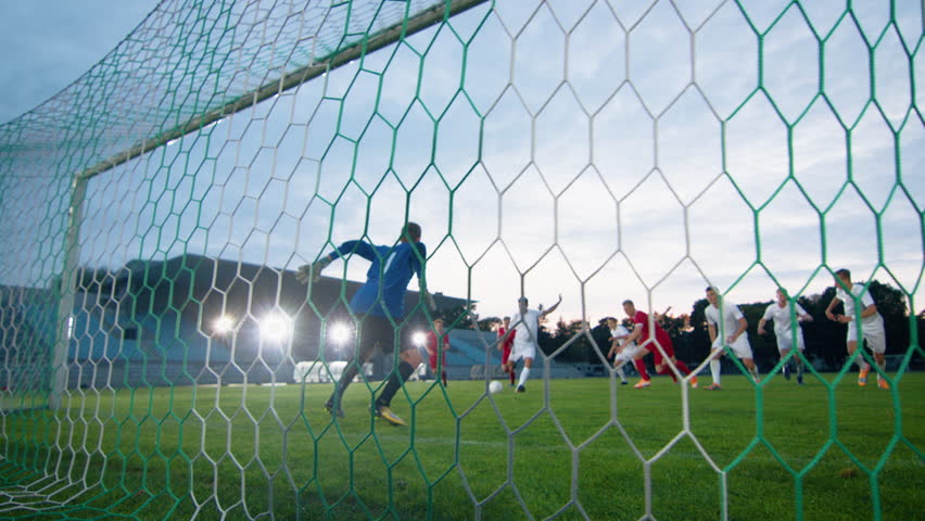 On Soccer Championship Player Kicks the Ball and Goalkeeper Tries to Defend Goals but Jumps and Fails to Catch the Ball. Camera Shot from Behind the Net with whole Stadium Visible. Royalty-Free Stock Footage #1019537881