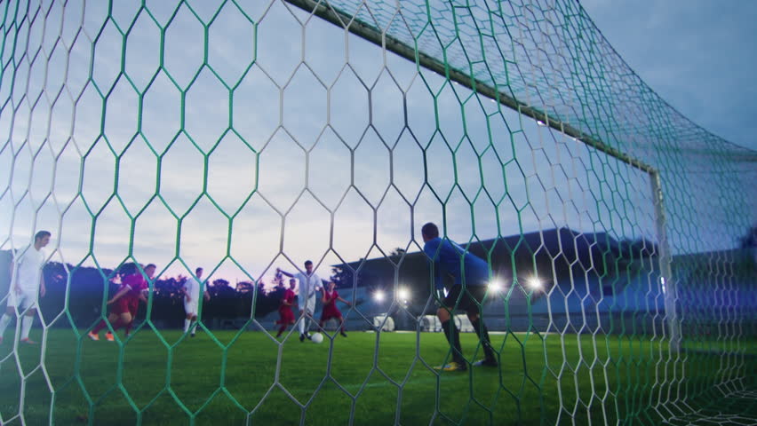 On Soccer Championship Player Kicks the Ball and Goalkeeper Tries to Defend Goals but Jumps and Fails to Catch the Ball. Camera Shot from Behind the Net with whole Stadium Visible. | Shutterstock HD Video #1019537884