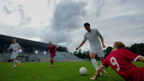 Professional Soccer Player Leads with a Ball, Masterfully Dribbling and Bypassing Sliding Tackles of His Opponents. Two Professional Football Teams Playing. Following Low Angle Shot.