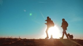 teamwork. two tourists hikers men and dog with backpacks at sunset go hiking trip. slow motion video. hikers adventure and the dog go walking. travel mountains silhouette. hikers lifestyle adventure
