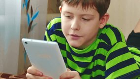 little boy are playing on the tablet lying on the bed. boy teen social media internet on a tablet indoors. children lifestyle and tablet concept