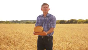 old farmer man baker holds a golden bread and loaf in ripe wheat field against the blue sky. slow motion video. harvest time. old man baker bread baking vintage agriculture concept. successful