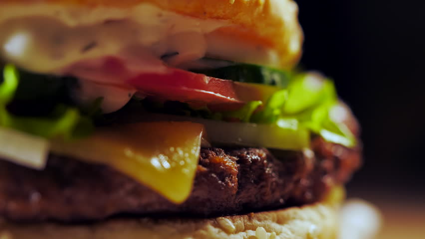 Big appetizing burger with meat cutlet, onion, vegetables, melted cheese, lettuce and mayonnaise sauce. Isolated hamburger rotates on dark smoke background, close-up view Royalty-Free Stock Footage #1019552995