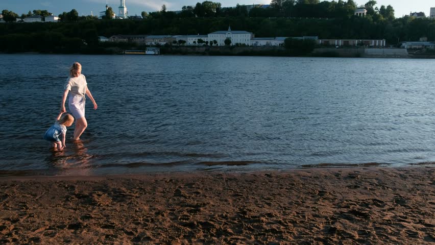 Mom and girl playing on the beach of the river at sunset and swim.