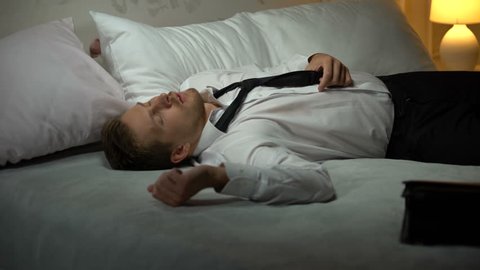 Man in business suit coming to hotel room drunk, falling to bed, alcoholism
