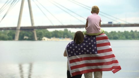 Family wrapped in American flag looking at bridge, immigration, independence day