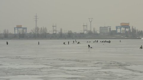 Many winter fishermen angling on ice of frozen water storage reservoir on background of hydro electric power station. Shot near Kiev, Ukraine on Dnieper river covered with ice and snow. 