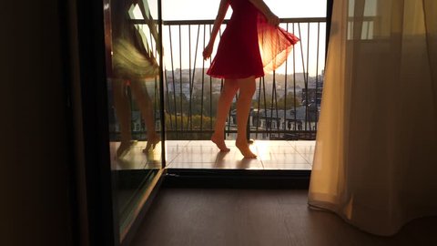 Excited woman spin in dance at balcony, enjoy happy morning time. Beautiful and merry moments, sun light flash behind, light red dress skirt fly around, slow motion shot