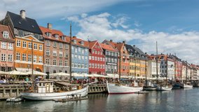 Nyhavn canal, one of the most important landmarks of Copenhagen. Colorful houses facades and sailing boats. Water reflection, sunny summer day.White clouds move across blue sky, time lapse video.