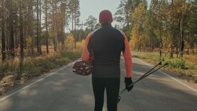 Training an athlete on the roller skaters. Biathlon ride on the roller skis with ski poles, in the helmet. Autumn workout. Roller sport. Adult man riding on skates. The athlete goes and holds sports