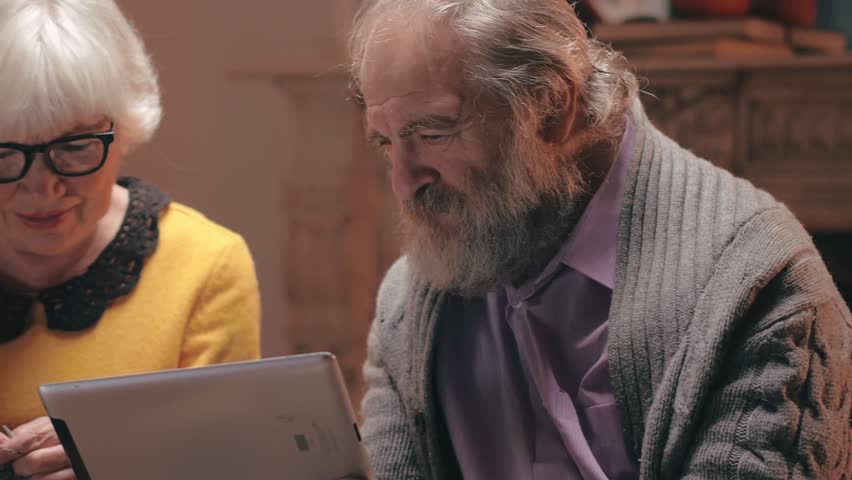 Positive elderly man and spouse old woman typing credit card information on the phone for payment in the online store while sitting in a cozy warm country house