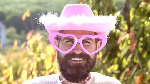 Comic man with funny hipster pink sunglasses and comic pink hat. Bearded crazy man looking at the camera. Make funny face. Cowboy