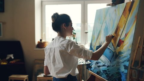 Serious female artist is working at picture using oil paints and palette-knife creating beautiful marine landscape on canvas. Painting technique and painters concept.