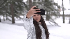 A young girl makes selfie using a smartphone while standing in a winter forest. slow motion HD