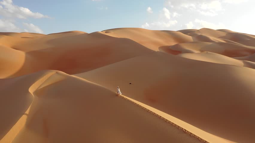Young woman in a white summer dress walking up on the side of a dune on a sunny afternoon. Abu Dhabi, UAE. Royalty-Free Stock Footage #1019621776