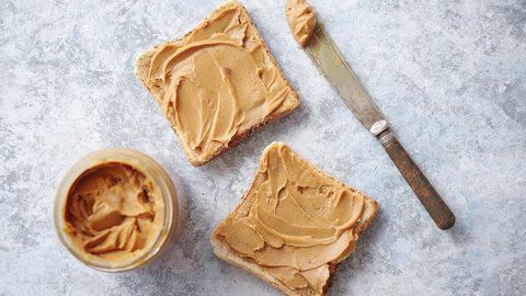 Two tasty peanut butter toasts placed on stone table with big jar. Knife on side. Above view.