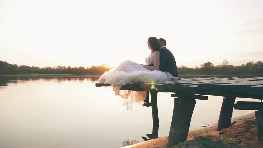 young couple in love near the river at sunset on the pier, the bride in a wedding dress with the groom