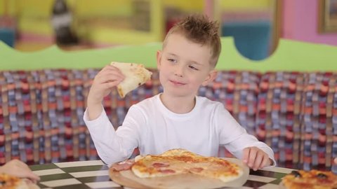 A little boy eats with pizza at the cafe, delicious food
