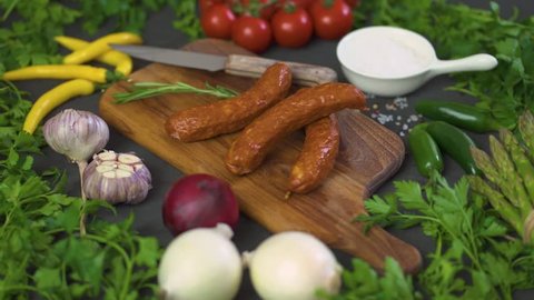 three delicious sausages with different vegetables on a wooden board, knife on a black table