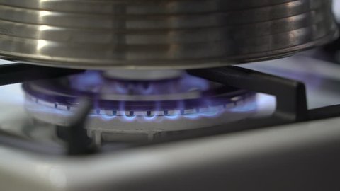 Heating up water in stainless steel kettle on gas stove. Burning blue flames of gas