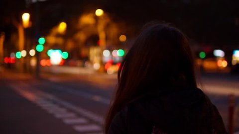 Young woman crossing the traffic road at night in the city centre alone.