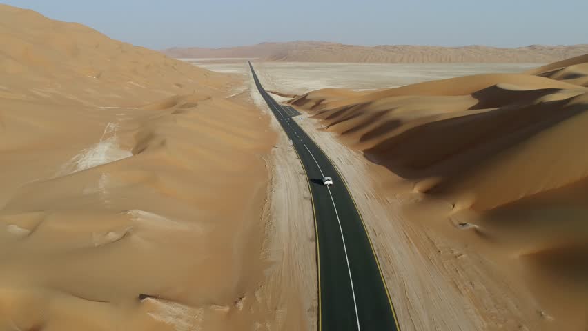 Aerial view of white car driving on road between dunes in the desert, Abu Dhabi, UAE.