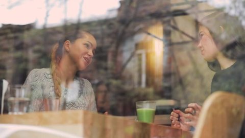 Women friends talking in a cafe behind the window