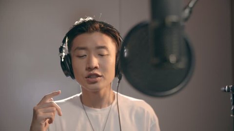 young asian singer singing in recording studio with headphone and microphone.