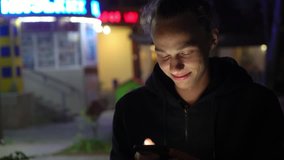 happy and positive young man surfing internet on mobile phone on the night steet, 4k