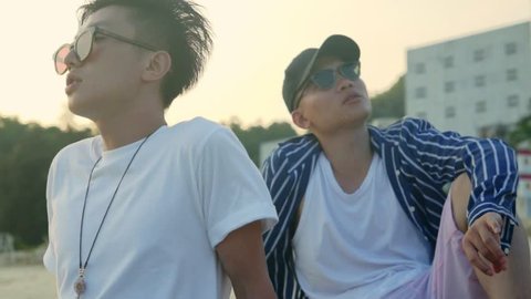 two young asian adult muscian sitting relaxing singing on beach, slow motion.