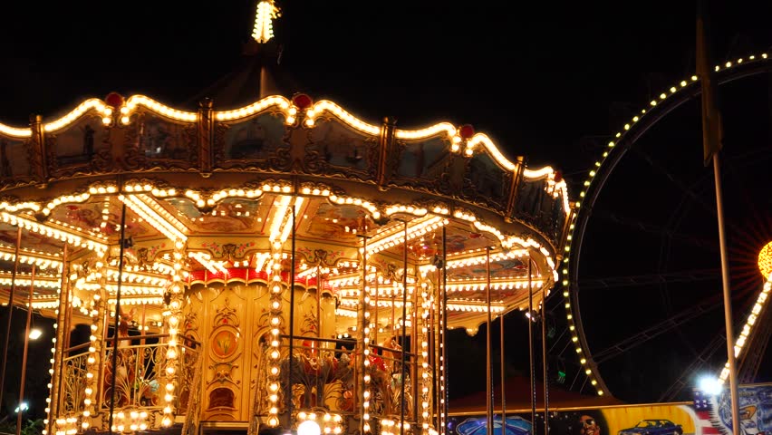 Fascinating flashing lights dark night sky illumination of vintage merry go round fair carousel ferris wheel at carnival