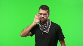 Man with glasses on green screen chroma key background listening to something by putting hand on the ear